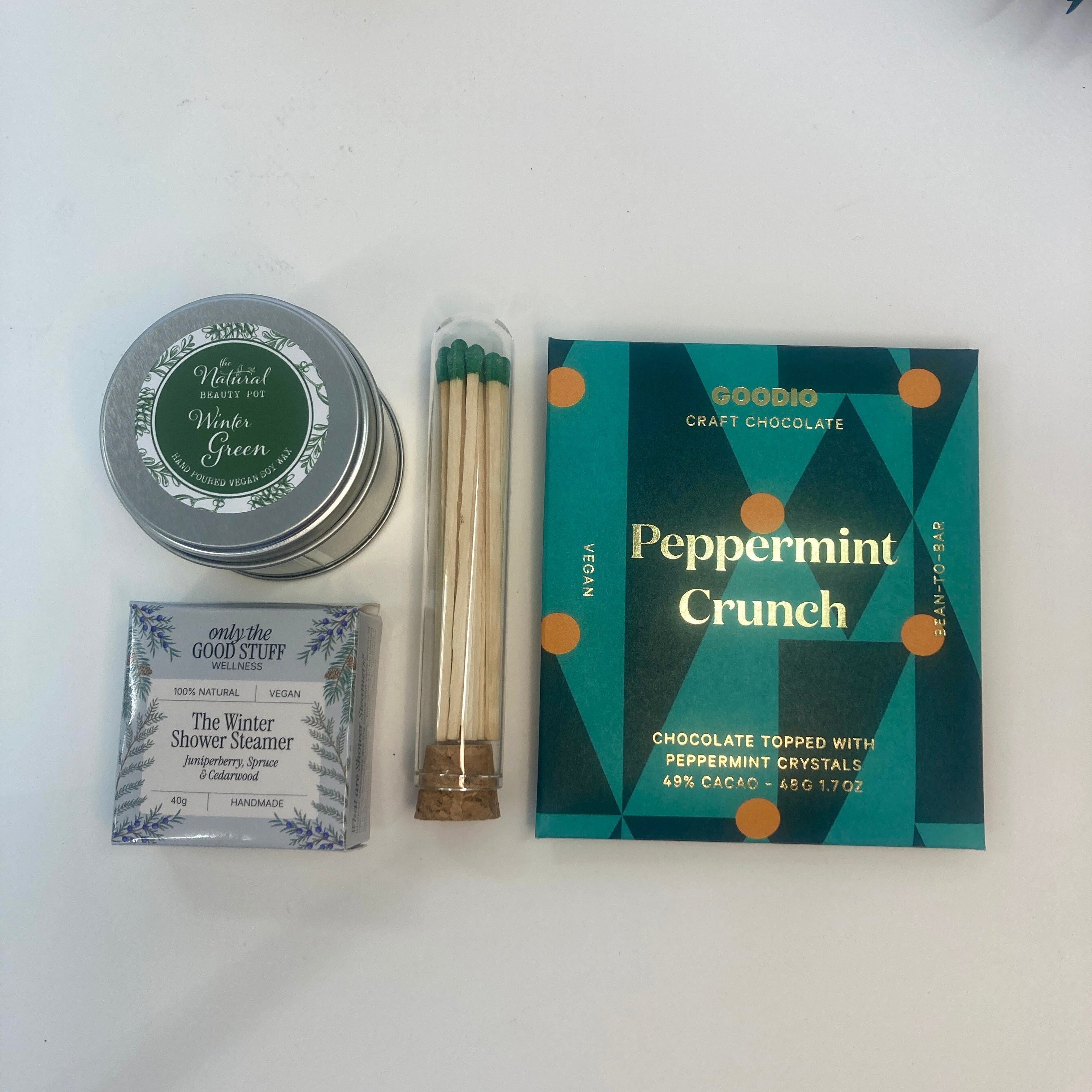 Collection of items including a tin, soap bar, matches, and a box of peppermint crunch chocolate on a white background.