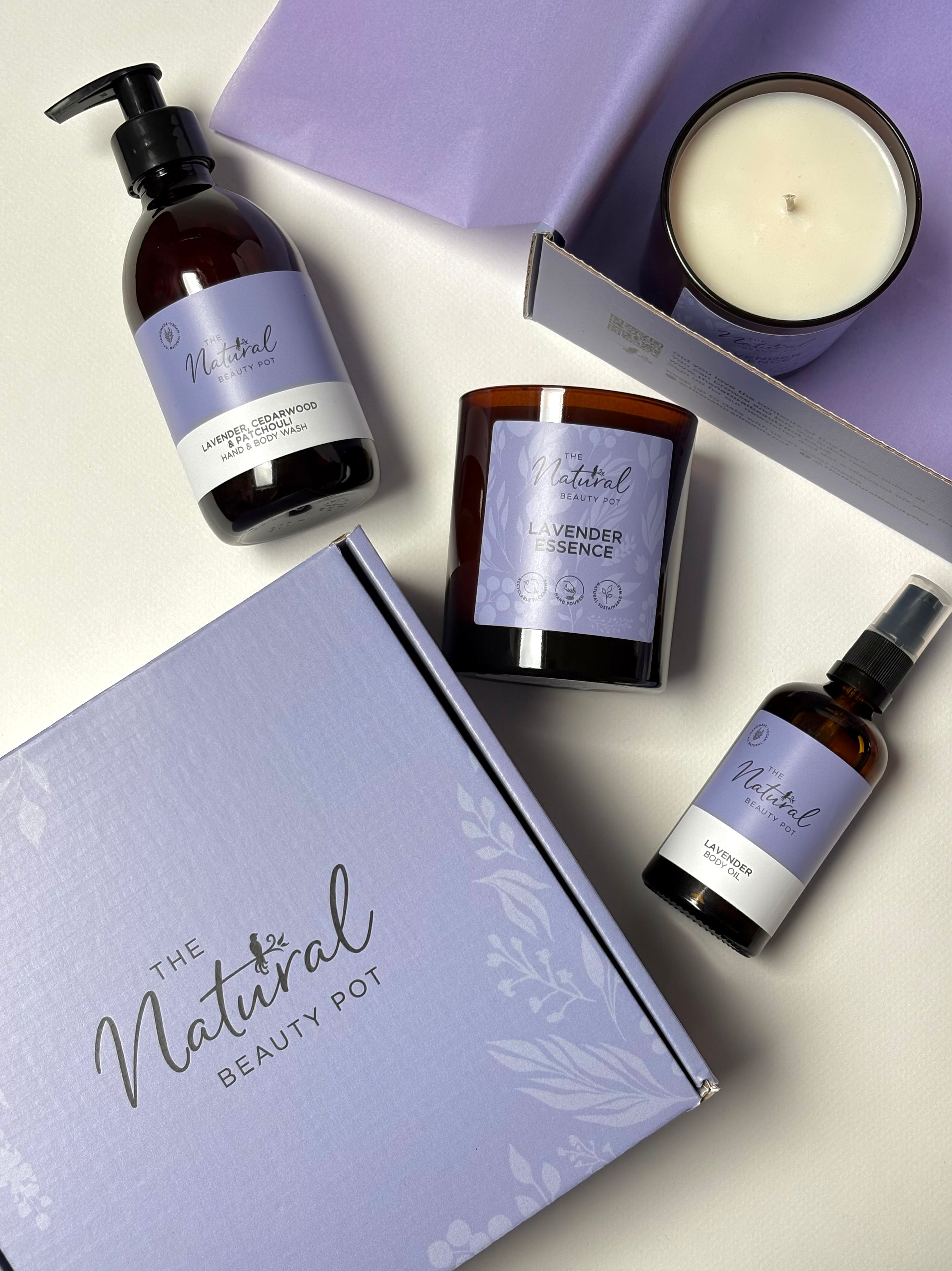 Collection of natural beauty products from 'The Natural Beauty Pot' in a lilac gift box, body oil, candle, hand and body wash in lavender