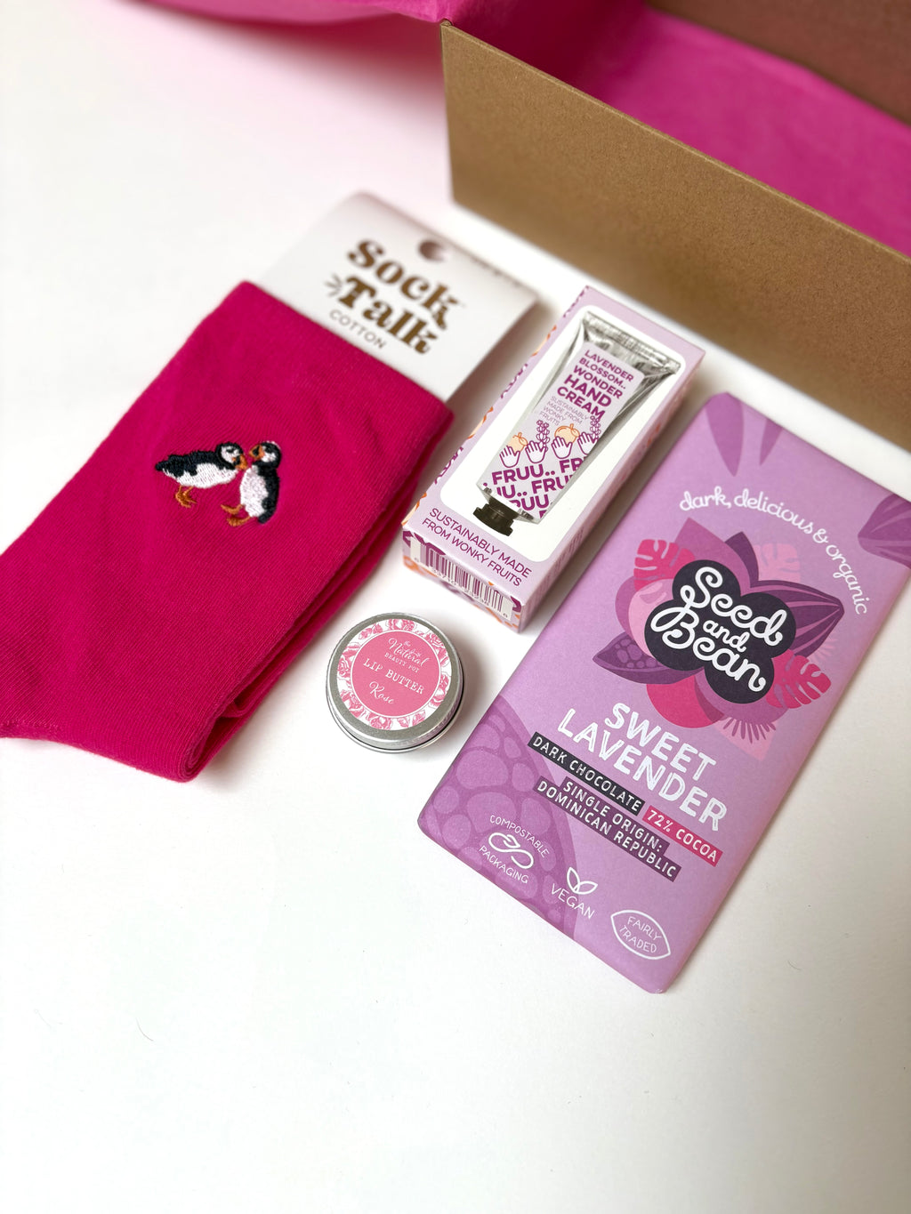 Collection of self care products  including a pink cotton socks, roses lip balm, lavender hand cream, and lavender chocolate