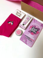 Collection of self care products  including a pink cotton socks, roses lip balm, lavender hand cream, and lavender chocolate