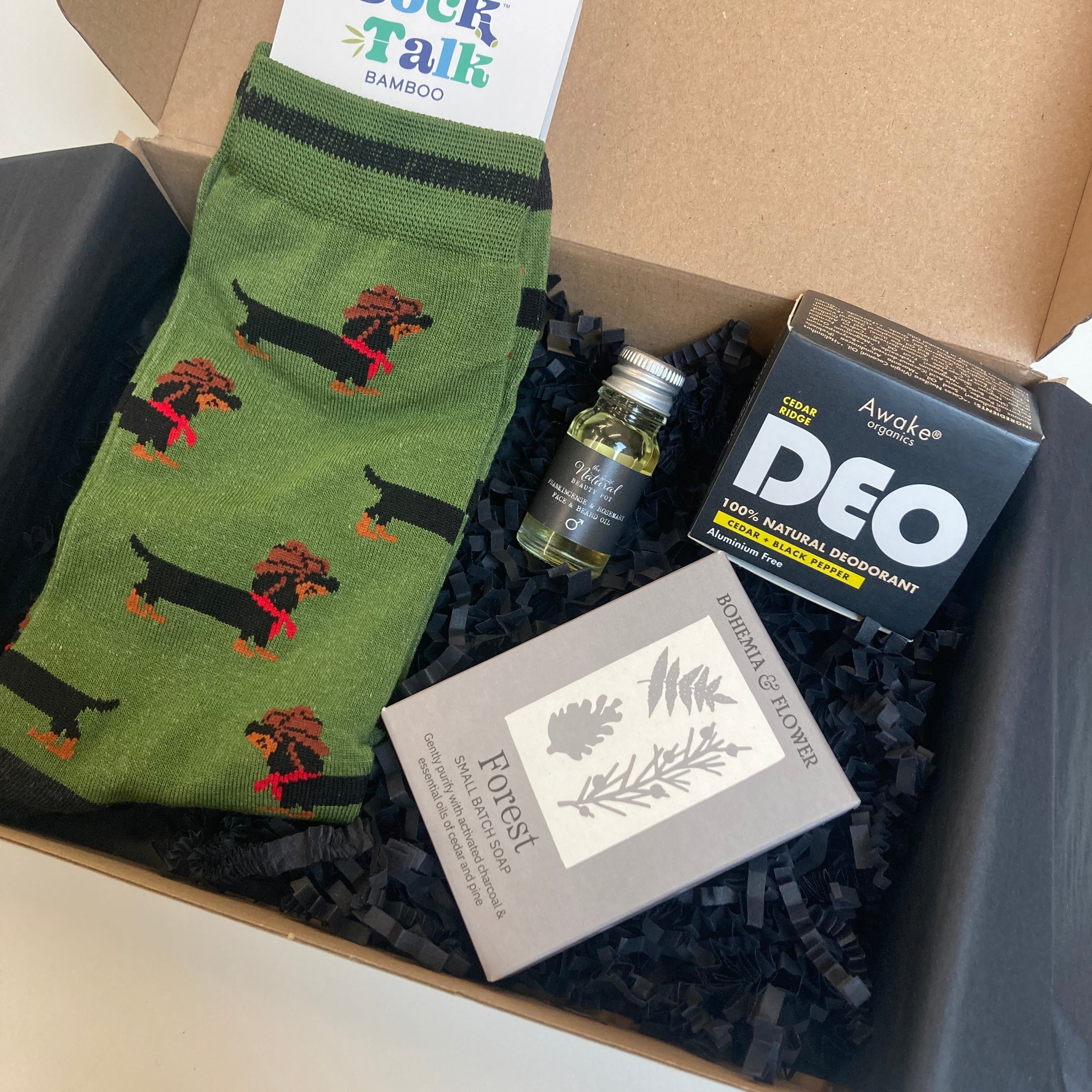 Box containing green socks with dog design, Box containing green socks with black and red designs, a natural mens deodorant, and a natural soap 
