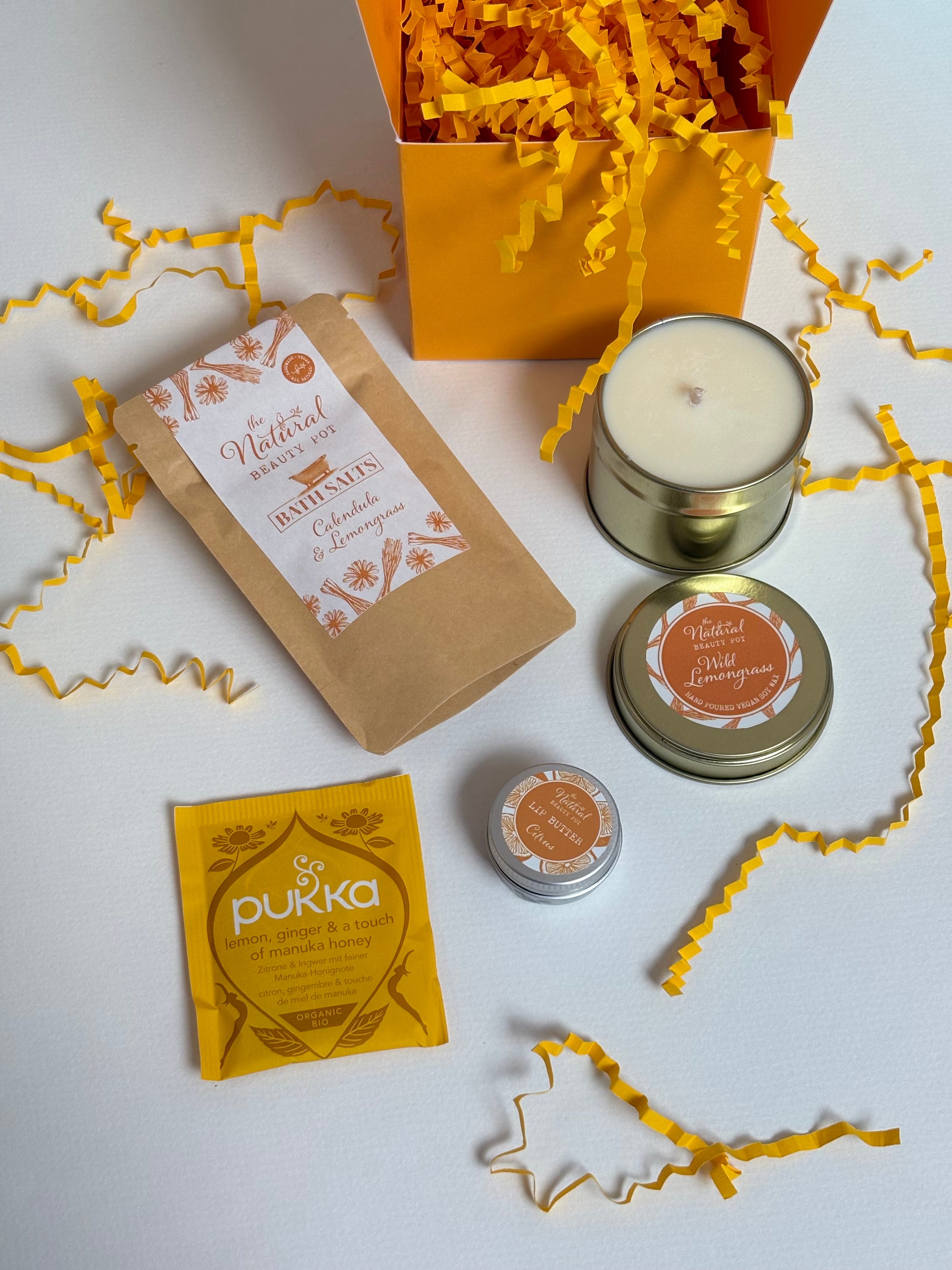 A yellow curated gift set featuring a Lemongrass & calendula Bath Salts sachet, a yellow Pukha tea, a small round lemongrass candle tin with yellow shredded paper and yellow gift box