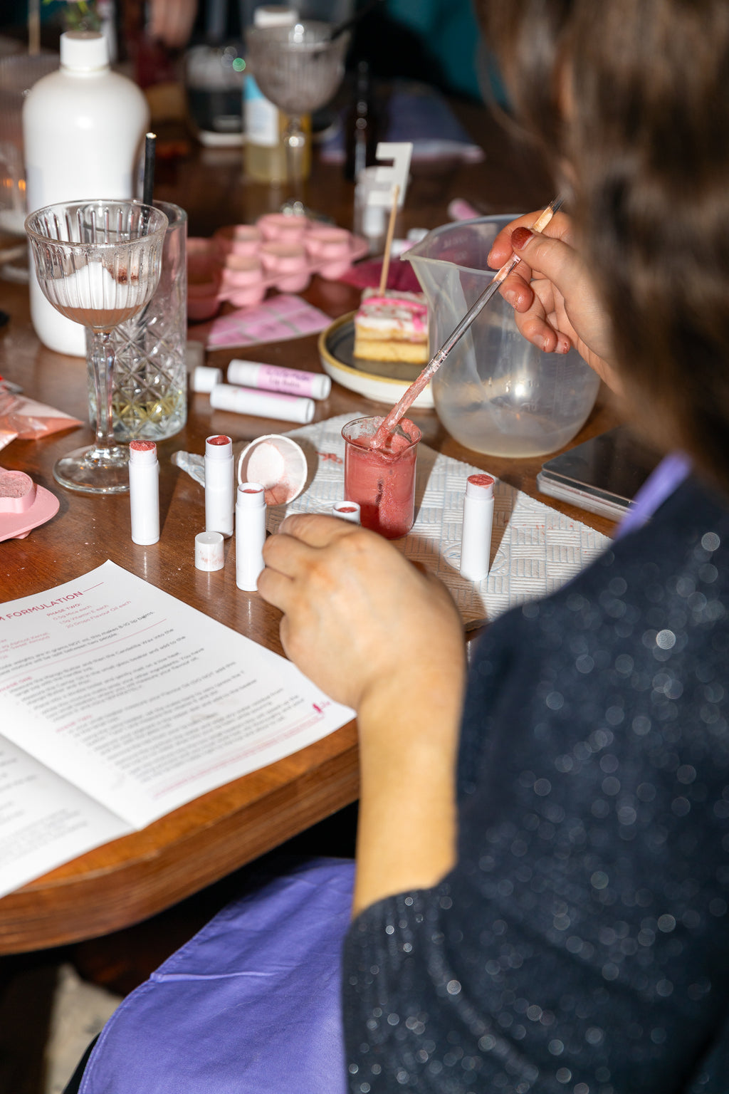 Person making natural lip balms at a table with various equipment on the table.