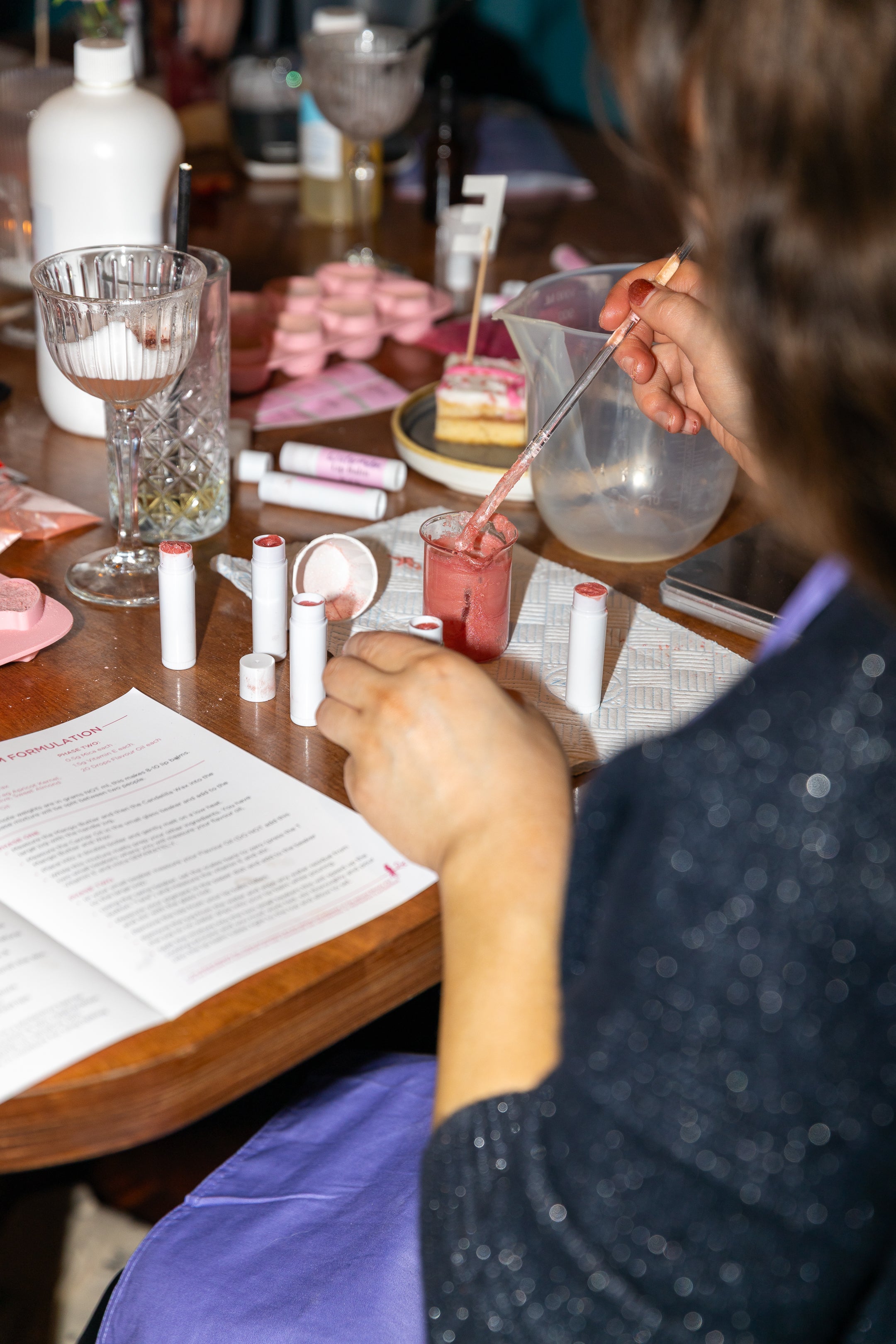 Person making natural lip balms at a table with various equipment on the table.