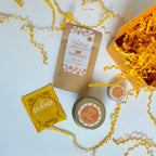 A curated gift set featuring a yellow gift box, Lemongrass & calendula Bath Salts sachet, a yellow Pukha tea, a small round lemongrass candle tin with yellow shredded paper.