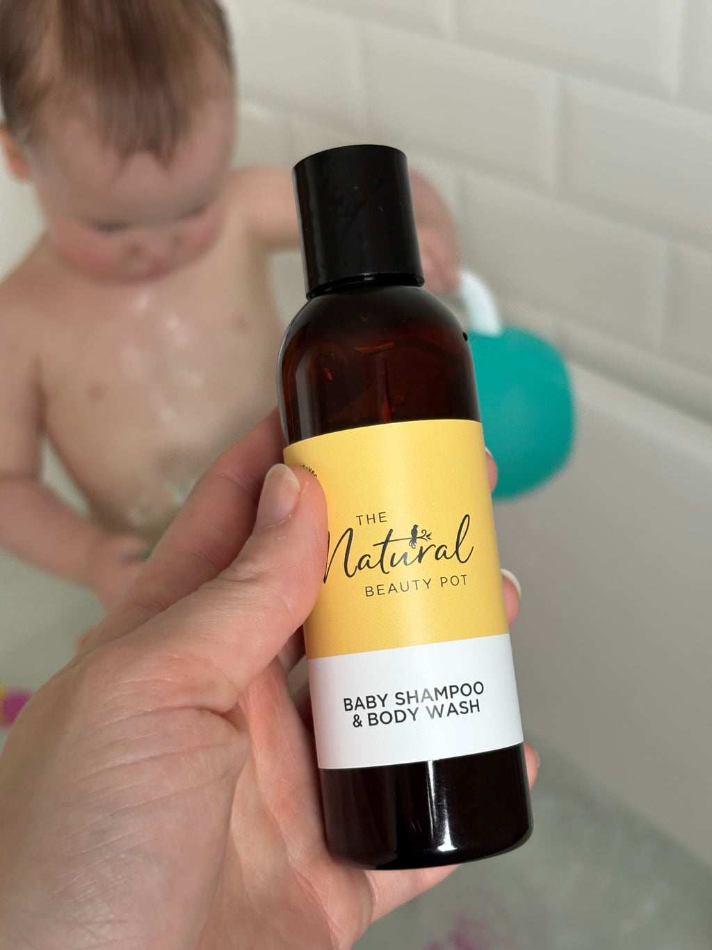 Baby shampoo and body wash bottle held by a hand with a child in the background