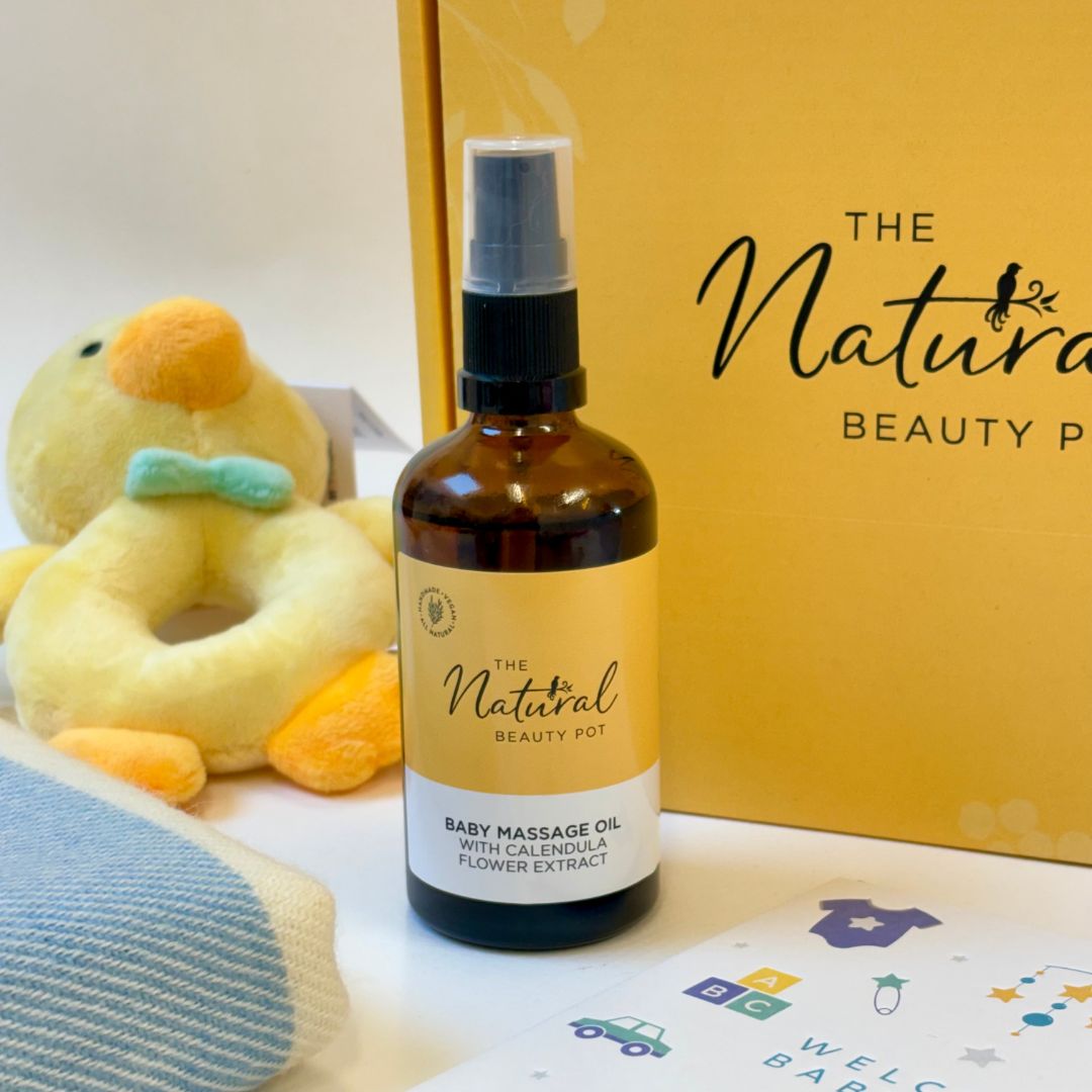 Baby massage oil bottle with 'The Natural Beauty Pot' branding, duck toy, and baby items in the background.