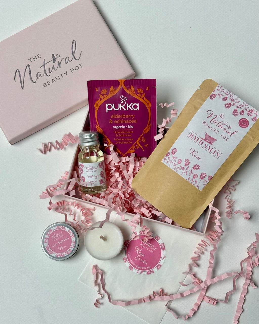 Collection of natural beauty products including a candle, tea, and bath salts in a pink gift box.