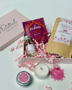 Collection of natural rose well being products including tea light candles, tea, bath salts, lip balm and skincare items on a light background with decorative ribbons.