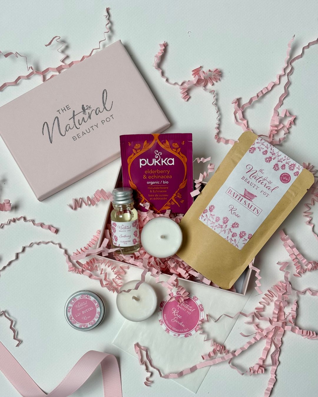 Self care gift box including candles, cleansing oil, bath salts and lip balm in a pink box 