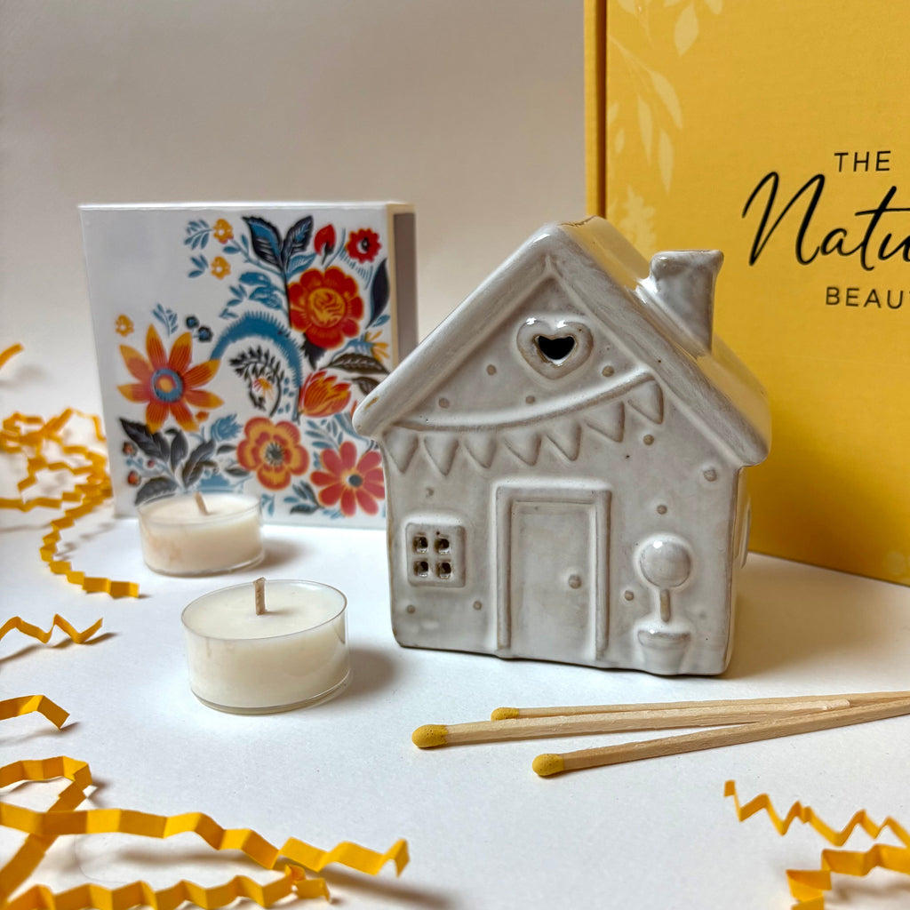 White ceramic house-shaped tea light  holder with candles and a box labeled 'The Natural Beauty Pot' 