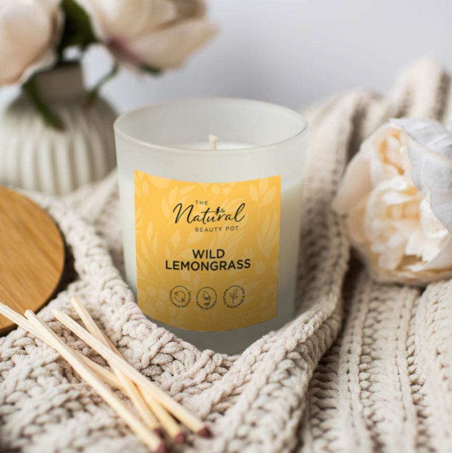 Candle with a yellow label wild lemongrass on a textured surface with flowers and wooden coaster.