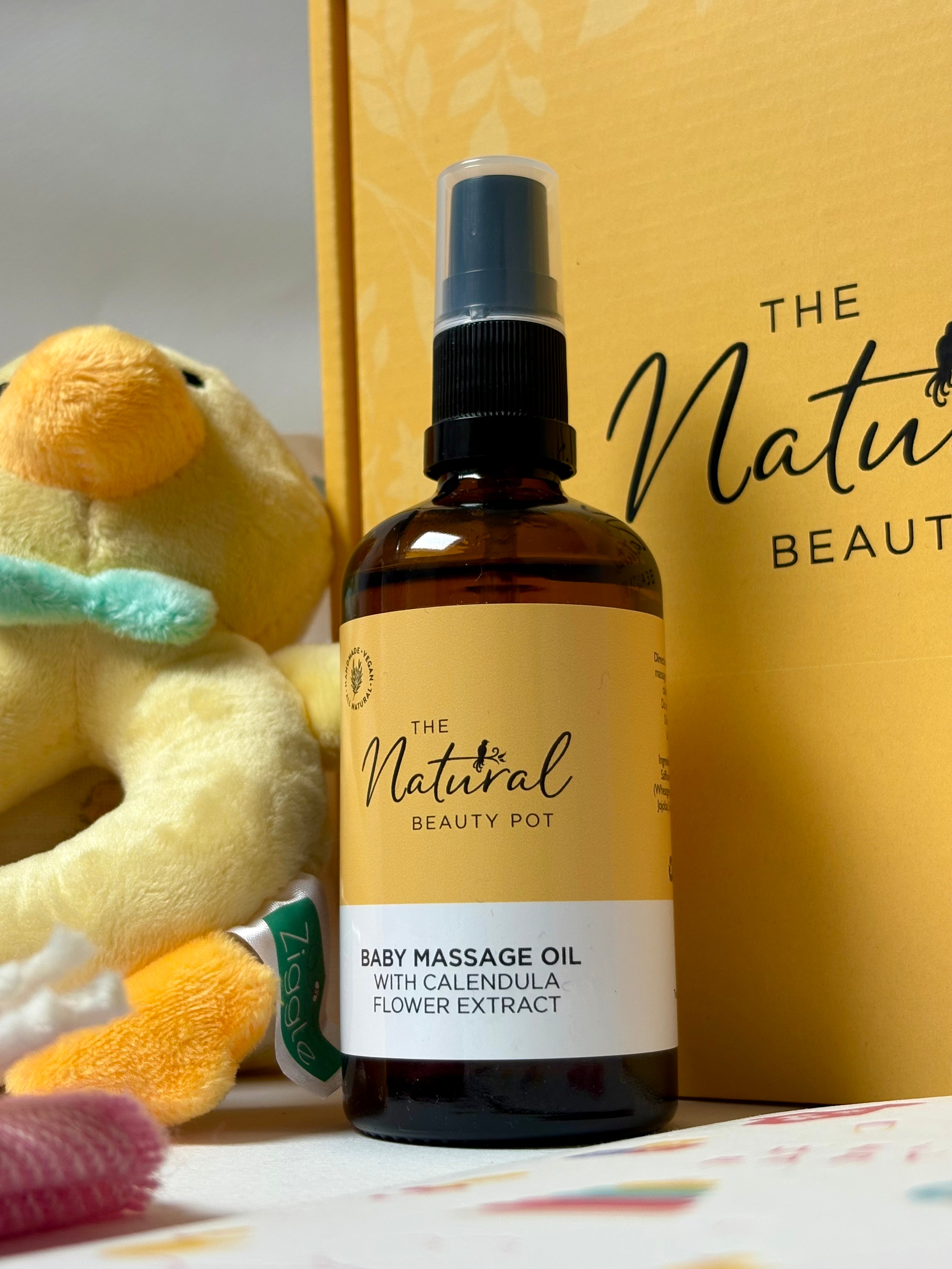 Baby massage oil bottle with 'The Natural Beauty Pot' branding, next to a plush toy and a box.