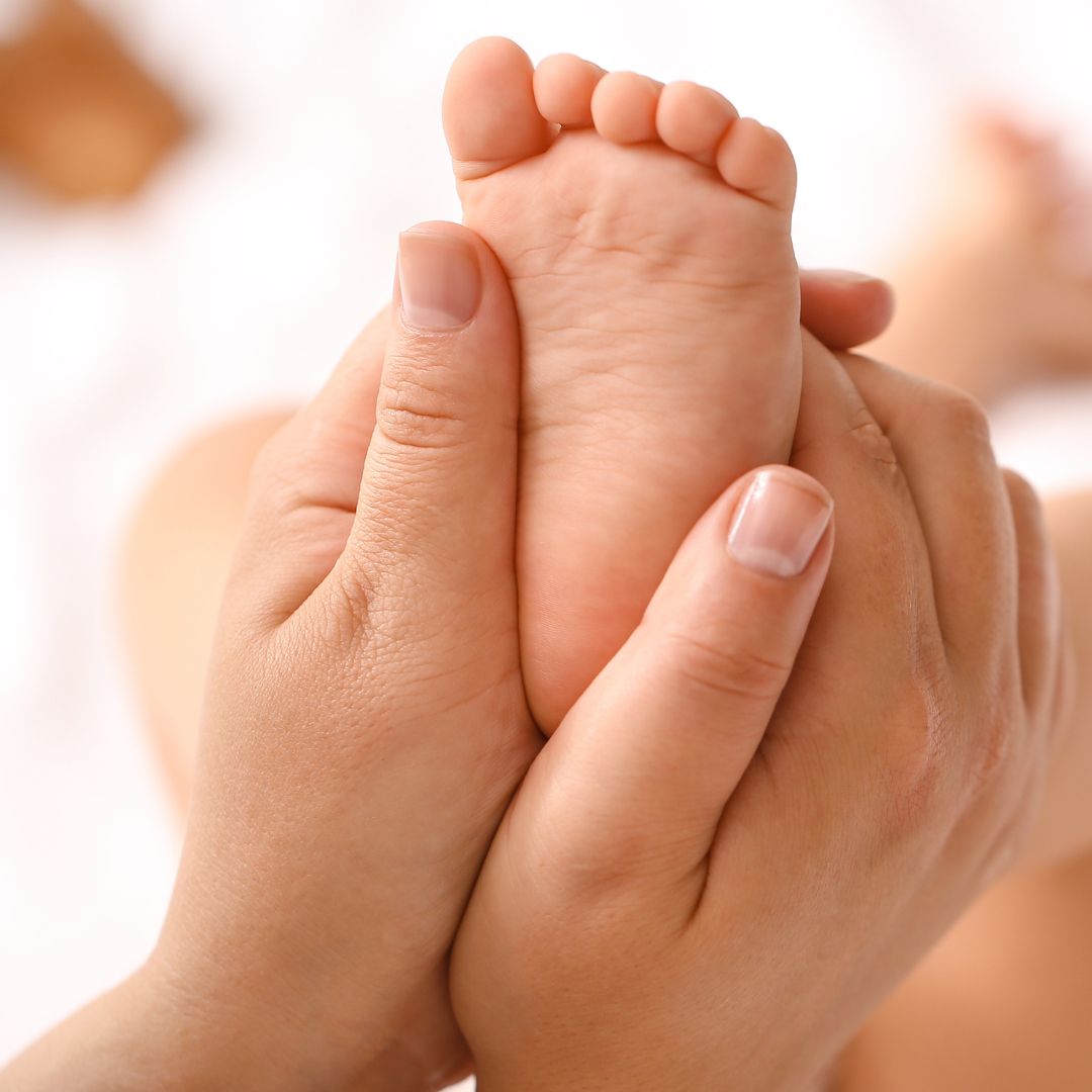 Close-up of a baby's foot being held by an adult hand for massage