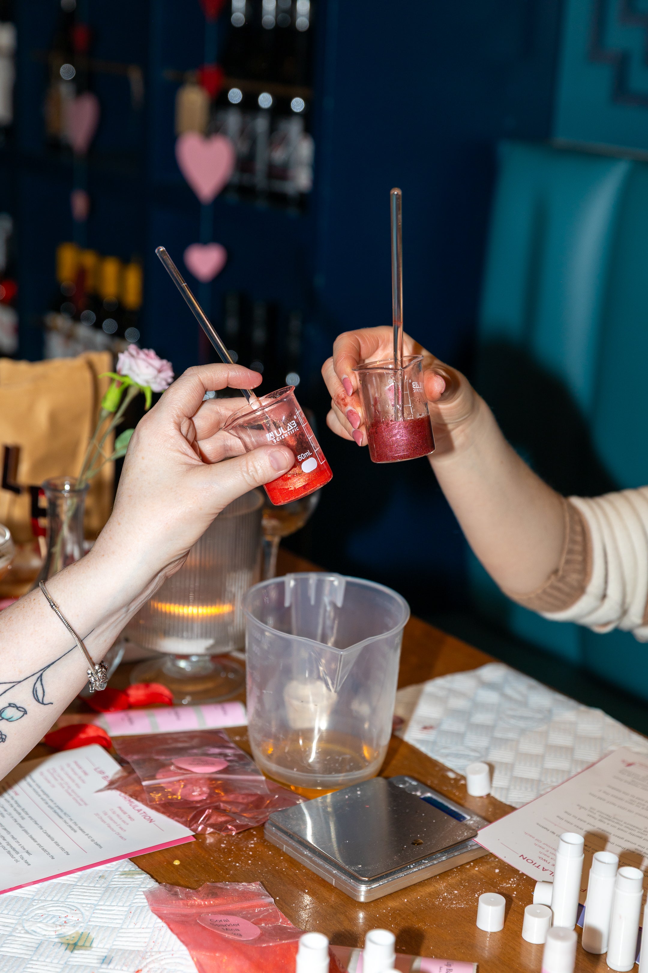 Two people clinking science beakers at a hen party making lip balms