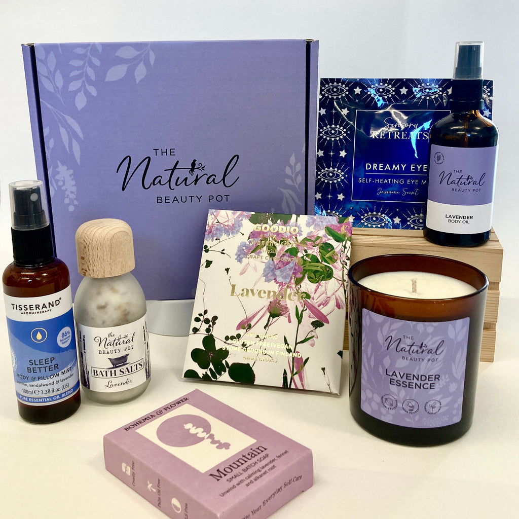 Collection of natural lavender beauty products including a candle, soap, and bottles in a purple gift box