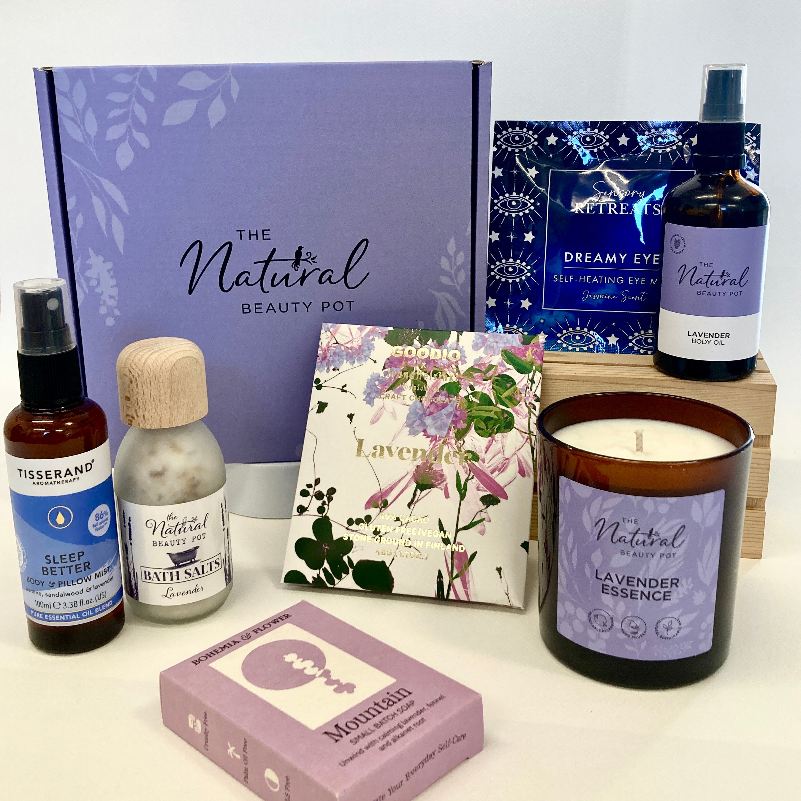 Collection of natural lavender beauty products including a candle, soap, and bottles in a purple gift box