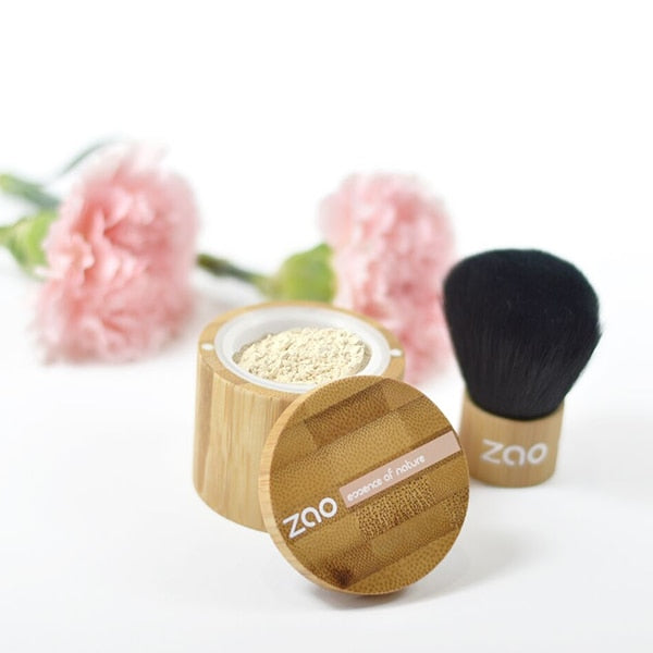Zao Mineral Silk Foundation container with a bamboo design and a Kabuki brush next to it, with flowers in the background.